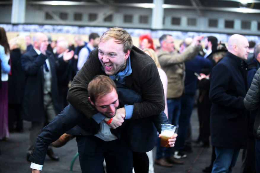 A Man In A Suit And Boots Celebrated A Big Win By Jumping On His Friend'S Back.